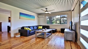 A modern living room with a black leather sofa, wooden coffee table, and a large window offering a view of trees.