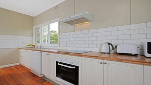 A kitchen with white cabinetry, a wooden countertop, a built-in oven, a microwave, and a kettle. - Culburra Sands – cosy cottage (Culburra Beach)