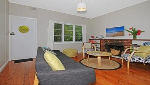 A living room with a sofa, ottoman, and a fireplace. - Culburra Sands – cosy cottage (Culburra Beach)