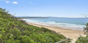 Una playa con valla de madera, vegetación y una vista despejada del océano.