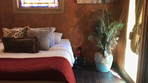 Un dormitorio con una cama, un vitral, un cuadro, una planta en maceta y una alfombra.