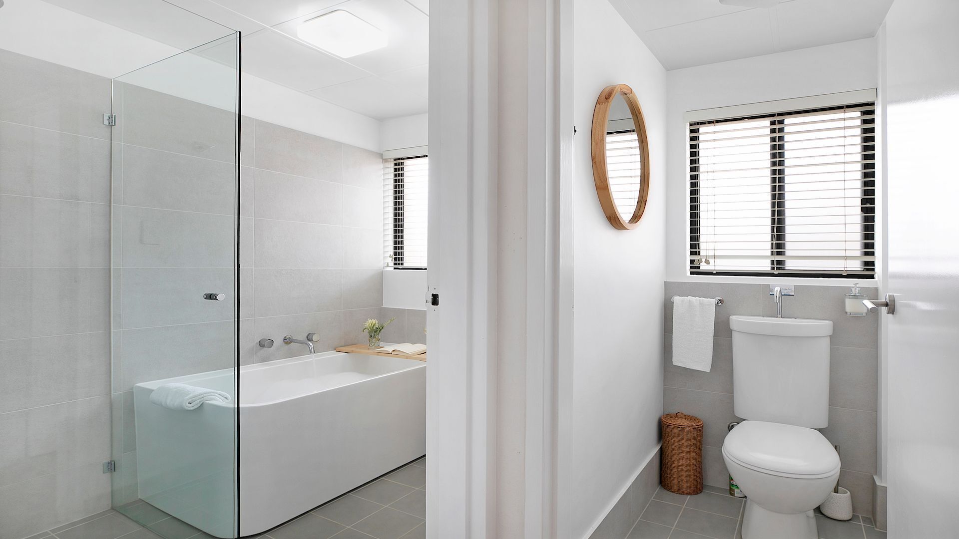 Un baño moderno con ducha de vidrio, una bañera independiente, inodoro y ventana con persianas.