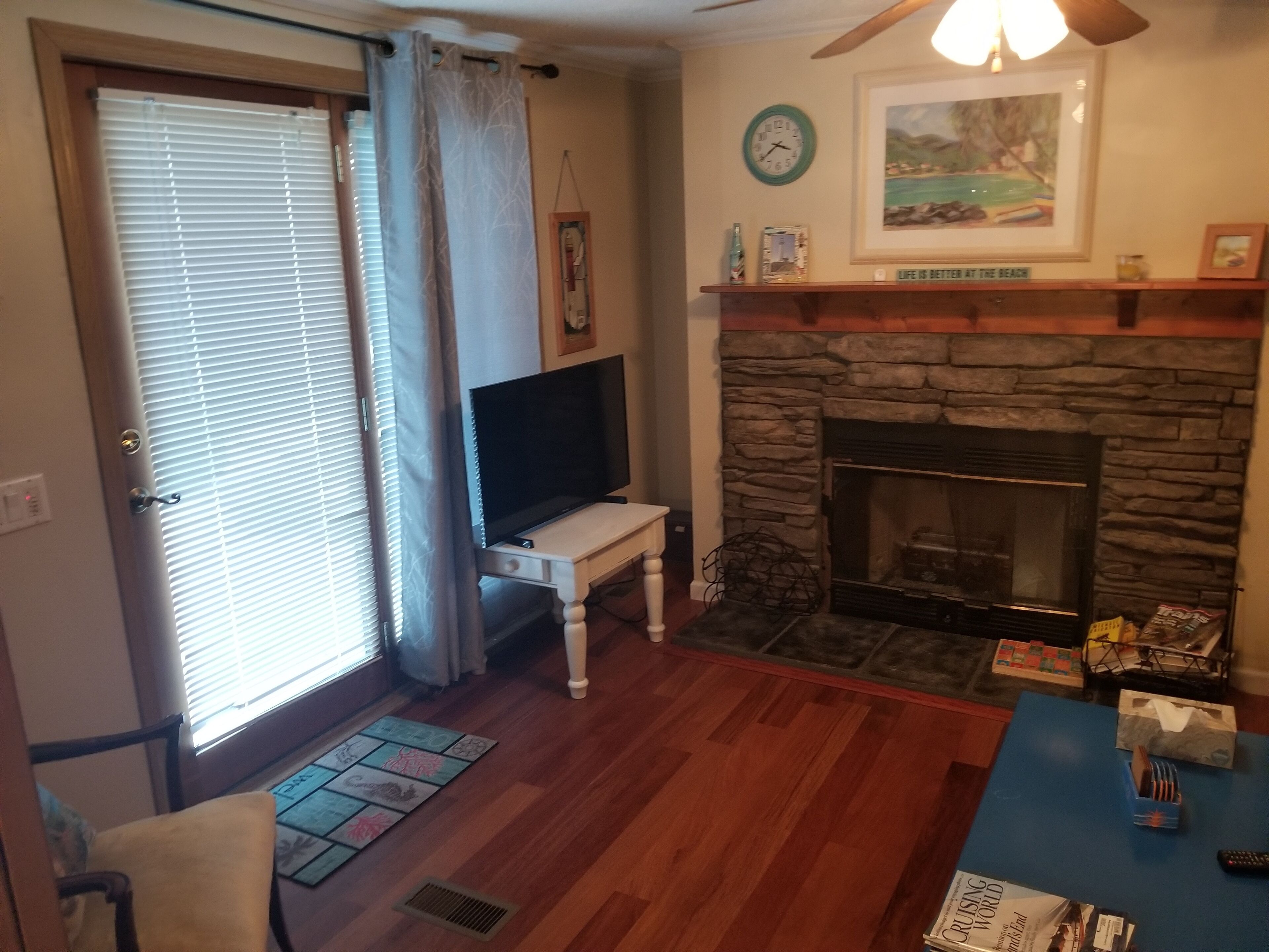 Una sala de estar con chimenea de piedra, un televisor sobre un mueble y una puerta con persianas.