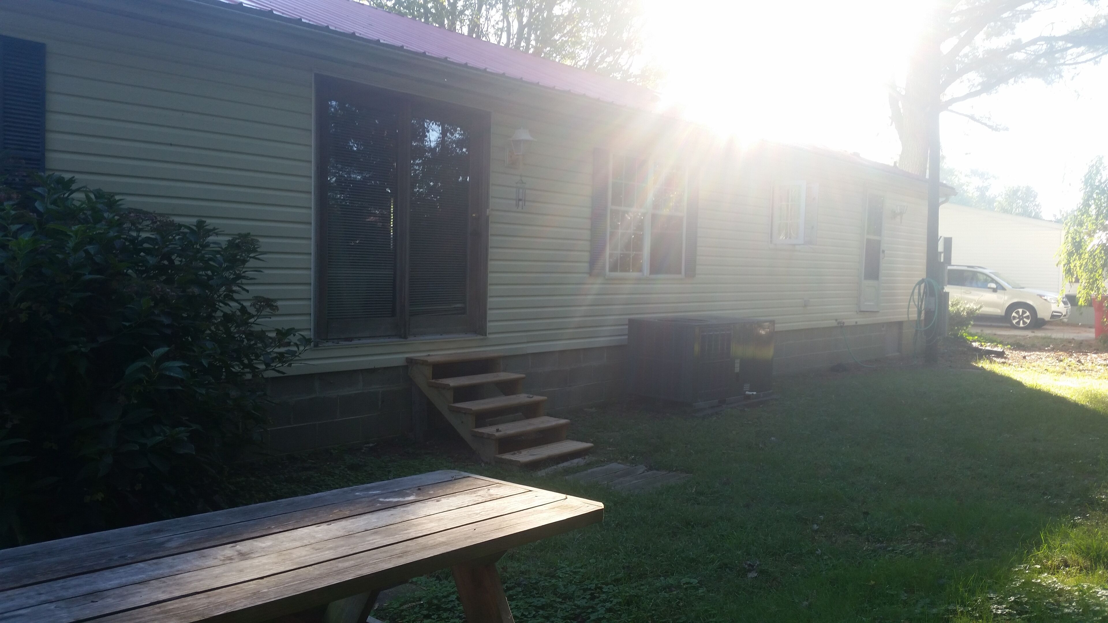 A mobile home with a front porch, a picnic table, and a vehicle parked nearby.