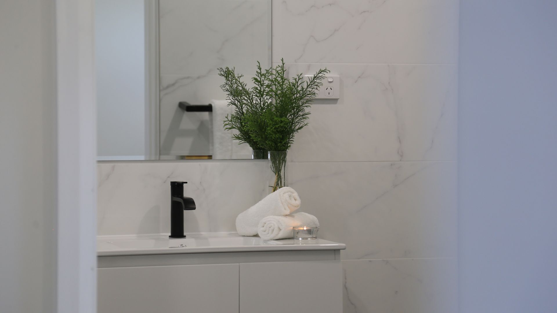 A bathroom with a white marble wall, a black faucet, a white towel, and a small plant in a glass vase.