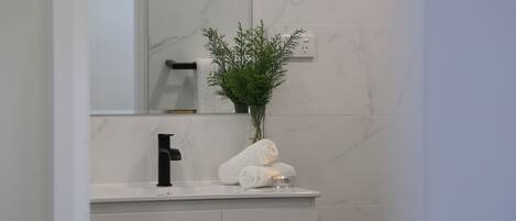 A bathroom with a white marble wall, a black faucet, a white towel, and a small plant in a glass vase.
