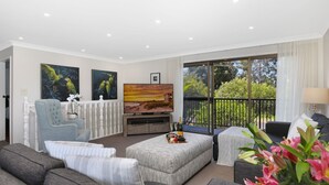 A modern living room with a television, seating, and a balcony with a view of greenery. - Ravello – Stay 3, Pay 2! (Callala Bay)