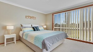 A bedroom with a large bed, two bedside tables, a view of the outdoors through a sliding glass door, and a 'RELAX' sign on the wall. - Cleveland Place - beach access (Culburra Beach)