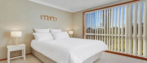 A bedroom with a large bed, two bedside tables with lamps, a view of the outdoors through a sliding door, and a 'RELAX' sign on the wall.