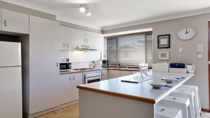 A modern kitchen with white cabinets, a central island, a microwave, and a coffee maker. - Cleveland Place - beach access (Culburra Beach)