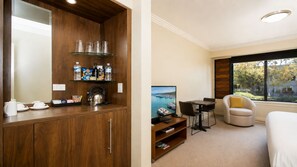 Quarto de hotel com um armário de madeira, televisão, sofá e janela com vista para barcos.