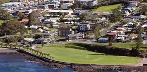 An aerial view of a residential area with houses, a large green park, and a rocky coastline.