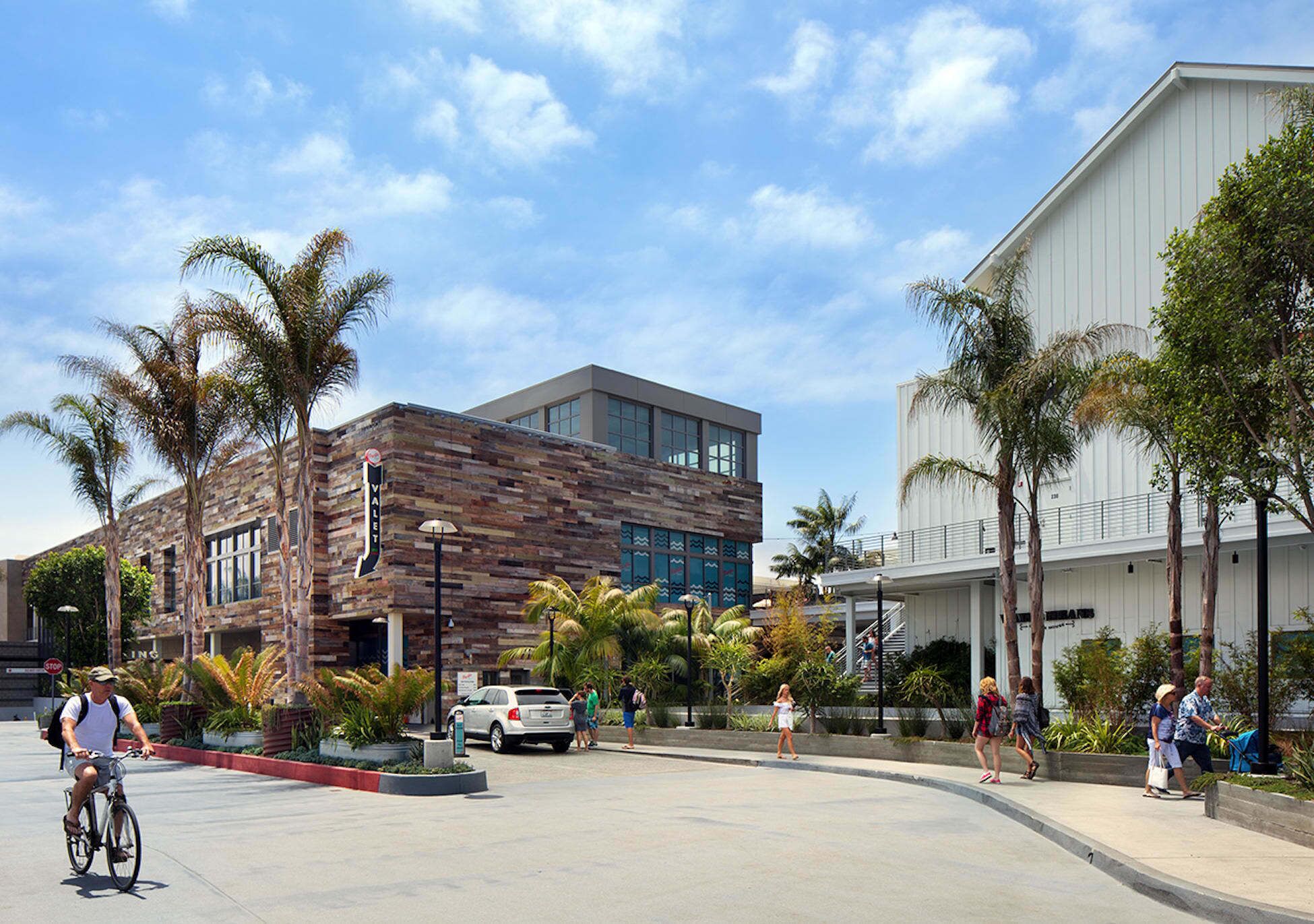 A modern building with a brick facade and large windows, surrounded by palm trees and a pedestrian walkway.