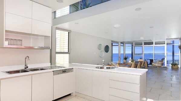 A modern kitchen with a central island, a dishwasher, and a large window overlooking the sea. - Albatross — a high set to ensure a perfect view (Culburra Beach)