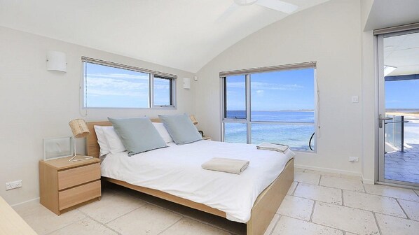 A bedroom with a bed, nightstands, and a view of the sea.