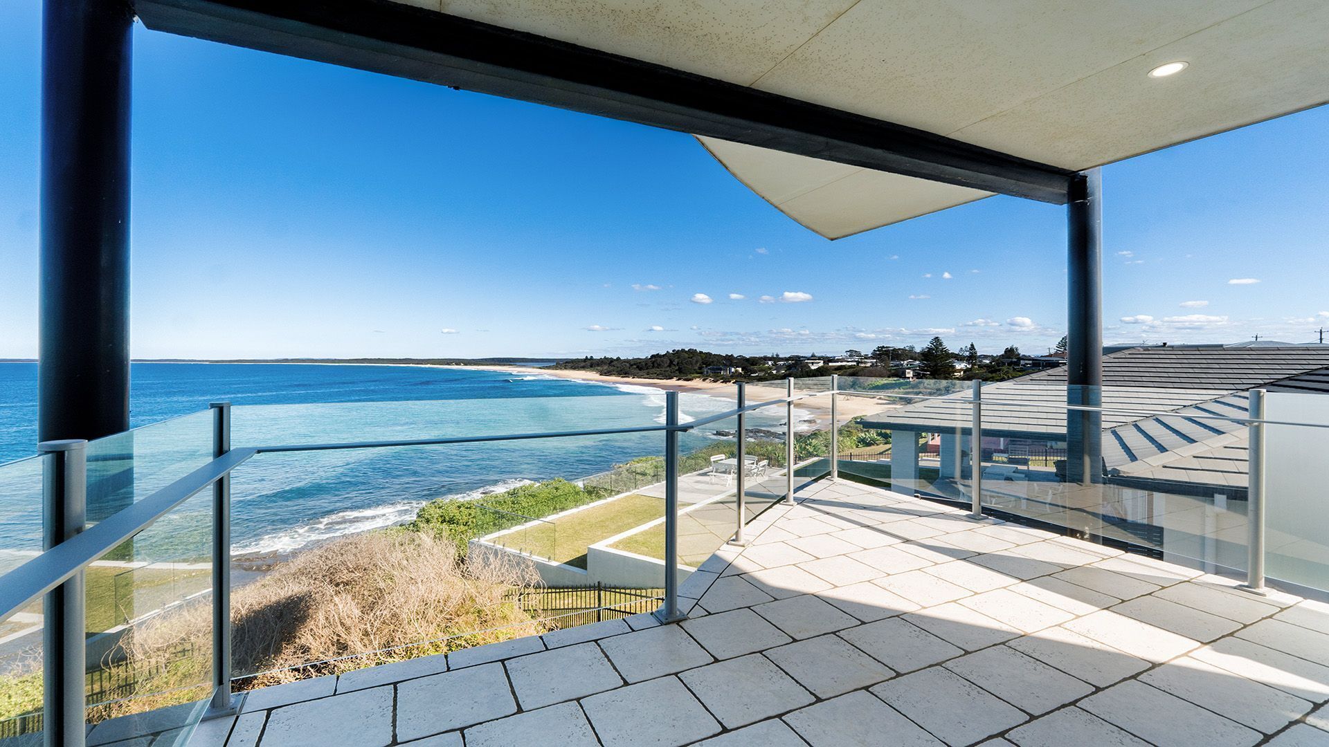 A balcony with a glass railing overlooking a beach and ocean.