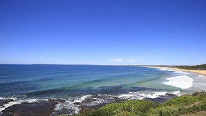 Un paysage côtier avec une plage de sable, une mer d’un bleu limpide et une côte rocheuse.