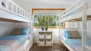 Dormitorio con literas, una ventana, una mesita con una planta y cajas de almacenamiento.