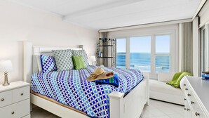 Een slaapkamer met een bed, nachtkastje, dressoir en uitzicht op de zee.