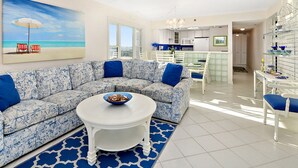 Een woonkamer met een gestreept bankstel, een ronde salontafel en een schilderij van een strandgezicht.