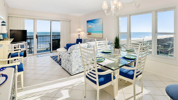 Een ruime woonkamer met een balkon met uitzicht op zee, een eettafel met stoelen en een televisie in de hoek.