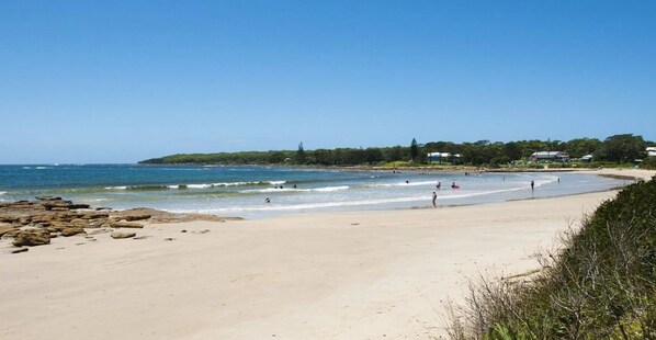 A beach with clear skies, calm waters, and a few people enjoying the shore. - Cudgee – one street back from the beach (Currarong)