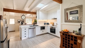 A modern kitchen with white cabinetry, a dishwasher, a microwave, and an oven. There's a wooden beam ceiling and a clock on the wall.