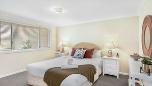 Een moderne slaapkamer met een groot bed, nachtkastjes, een spiegel en een raam met jaloezieën.