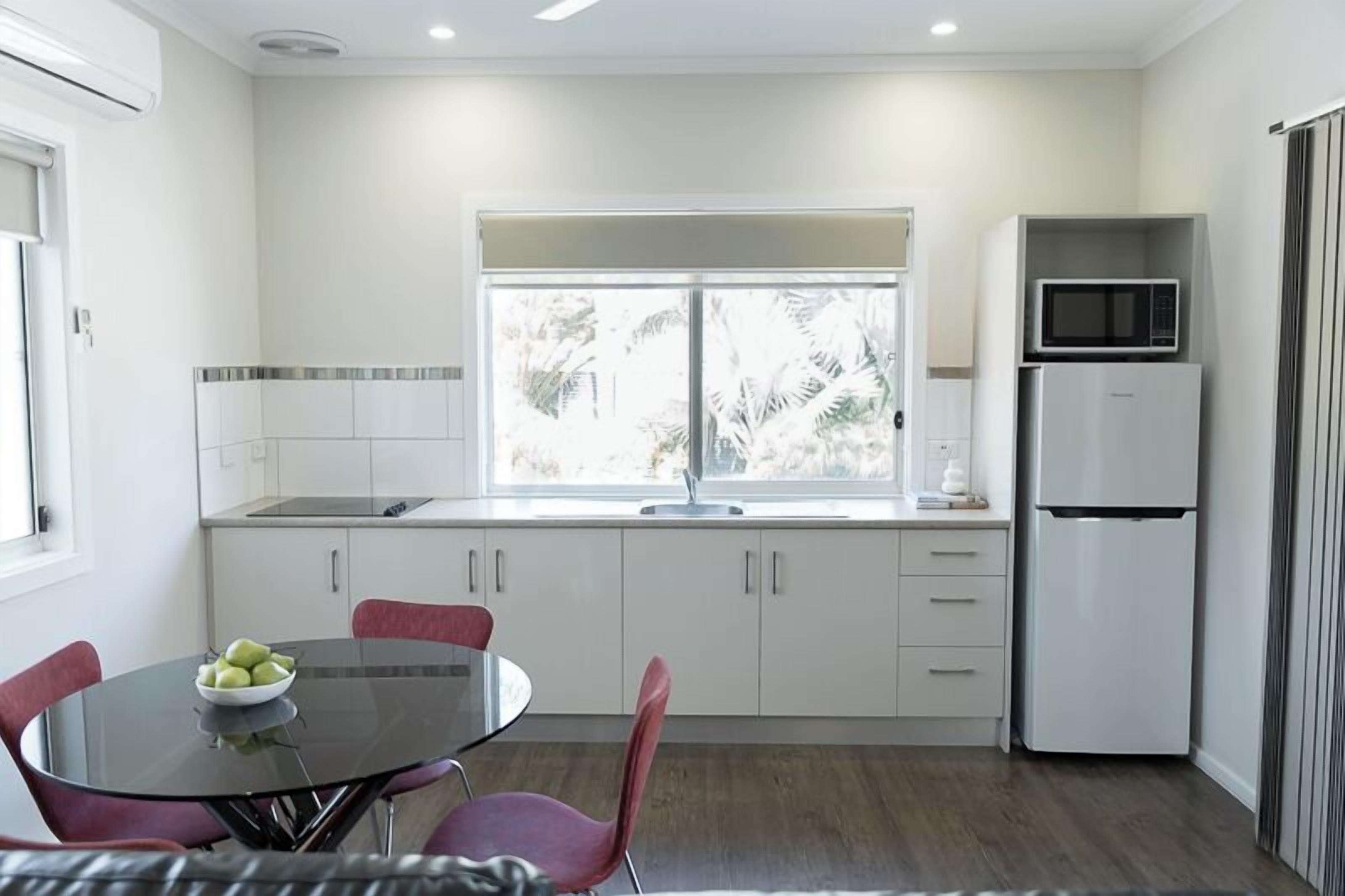A modern kitchen with white cabinets, a black dining table, and a refrigerator.