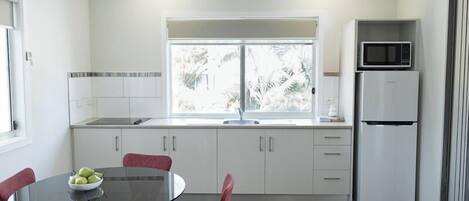 A modern kitchen with white cabinets, a black dining table, and a refrigerator.