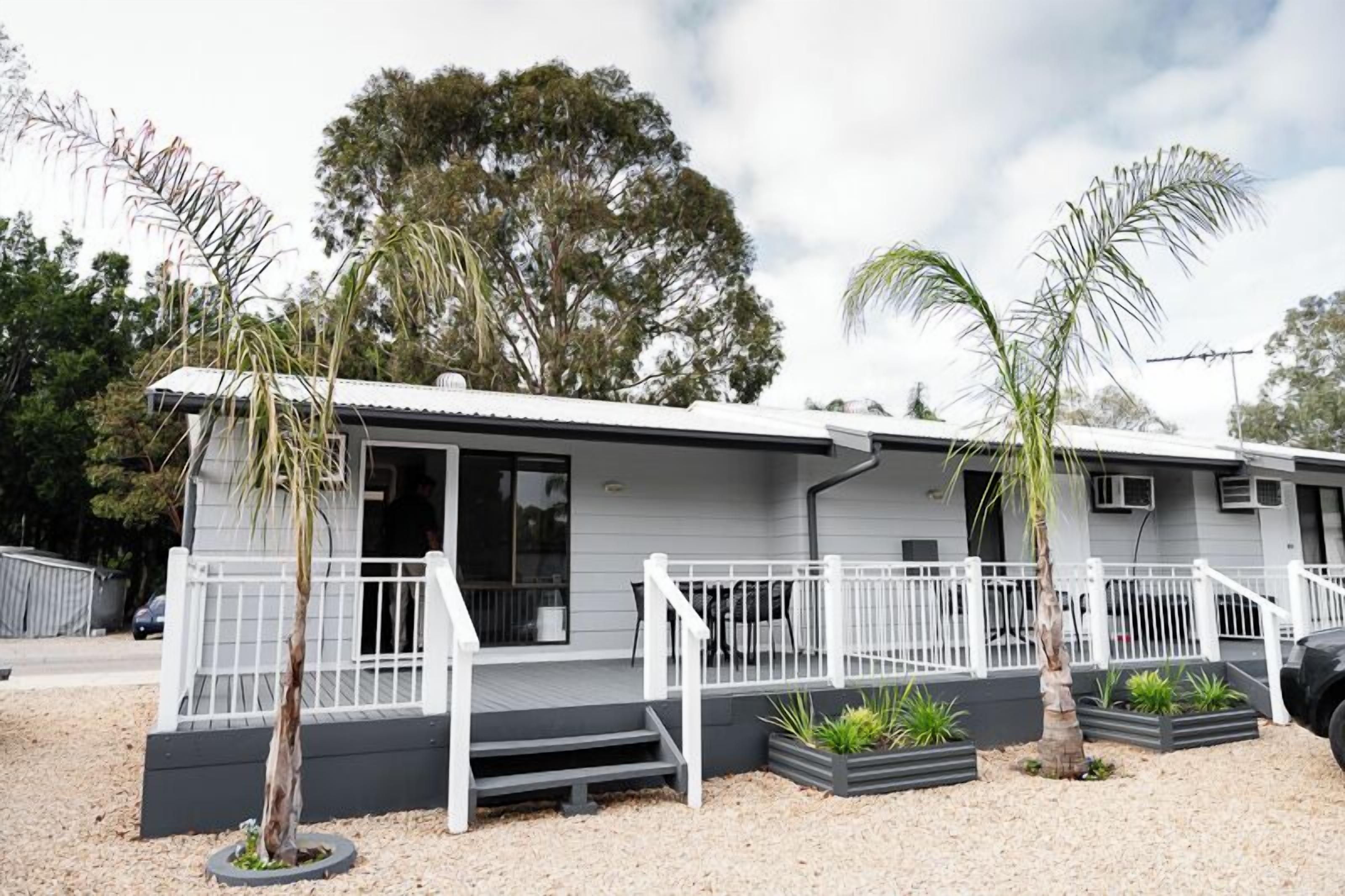 A two-story mobile home with a porch, white railings, and a gravel driveway.