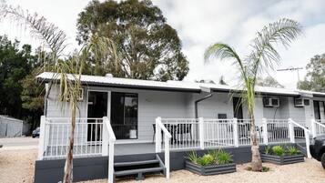 A two-story mobile home with a porch, white railings, and a gravel driveway.