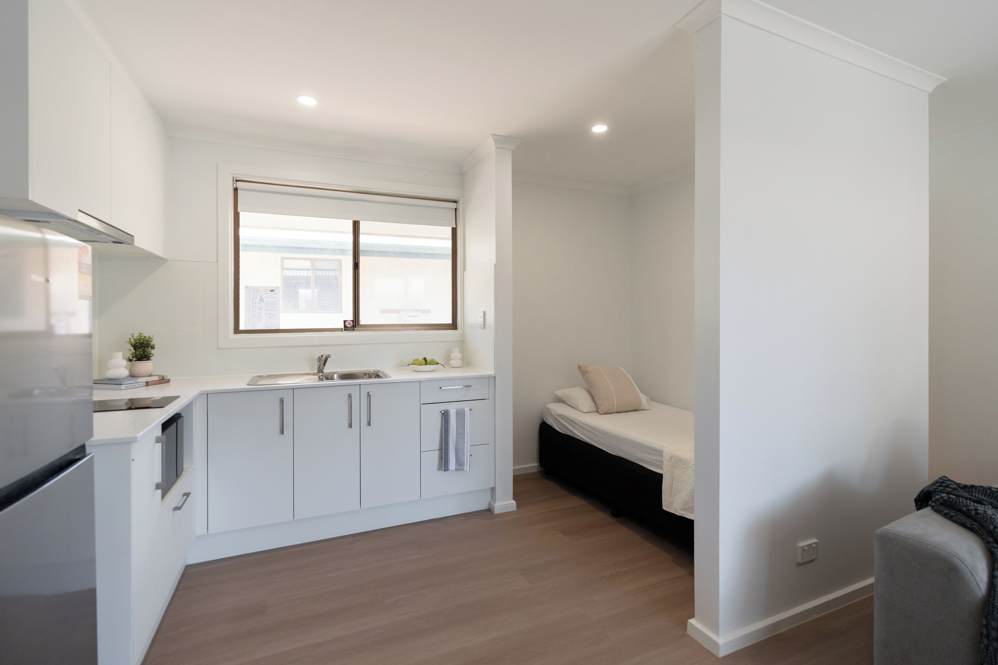 A compact kitchen with white cabinets, a built-in oven, and a window with blinds.