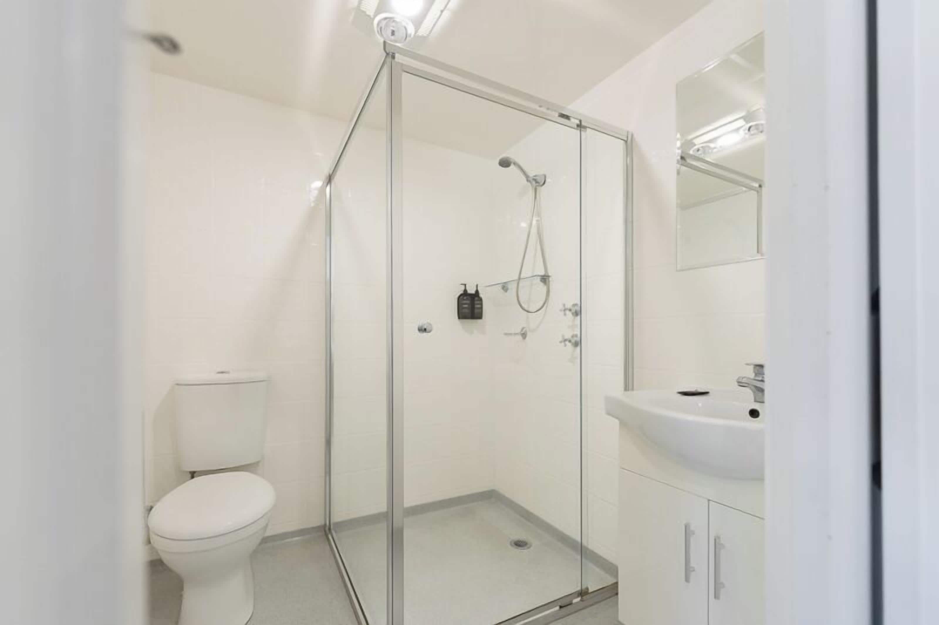 A modern bathroom with a glass-enclosed shower, a white toilet, and a sink with a mirror above it.