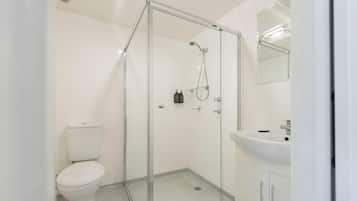 A modern bathroom with a glass-enclosed shower, a white toilet, and a sink with a mirror above it.