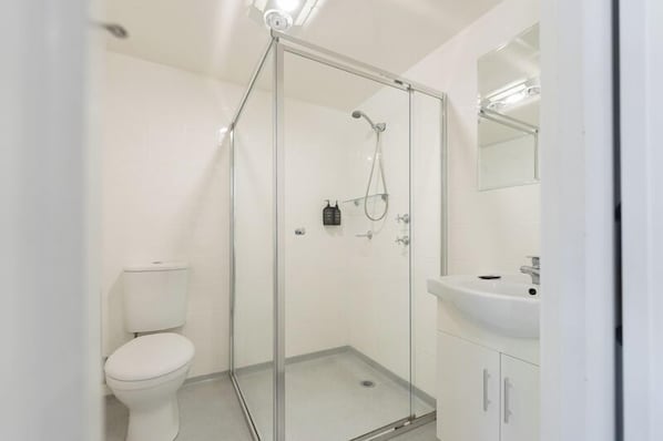 Um banheiro moderno com chuveiro em box de vidro, vaso sanitário branco e pia com espelho acima.