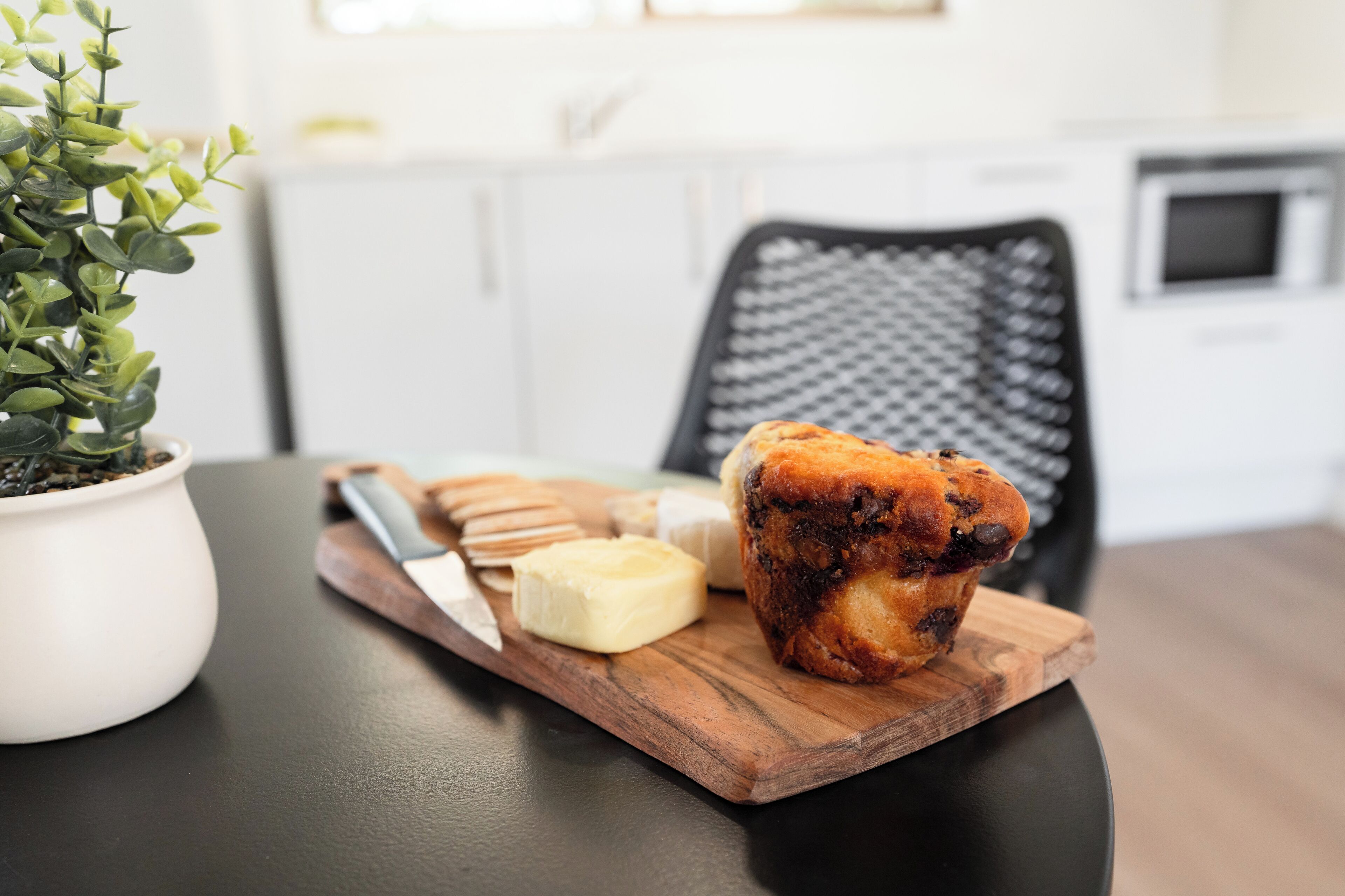 A wooden board with a muffin, a knife, and a butter knife on a table.