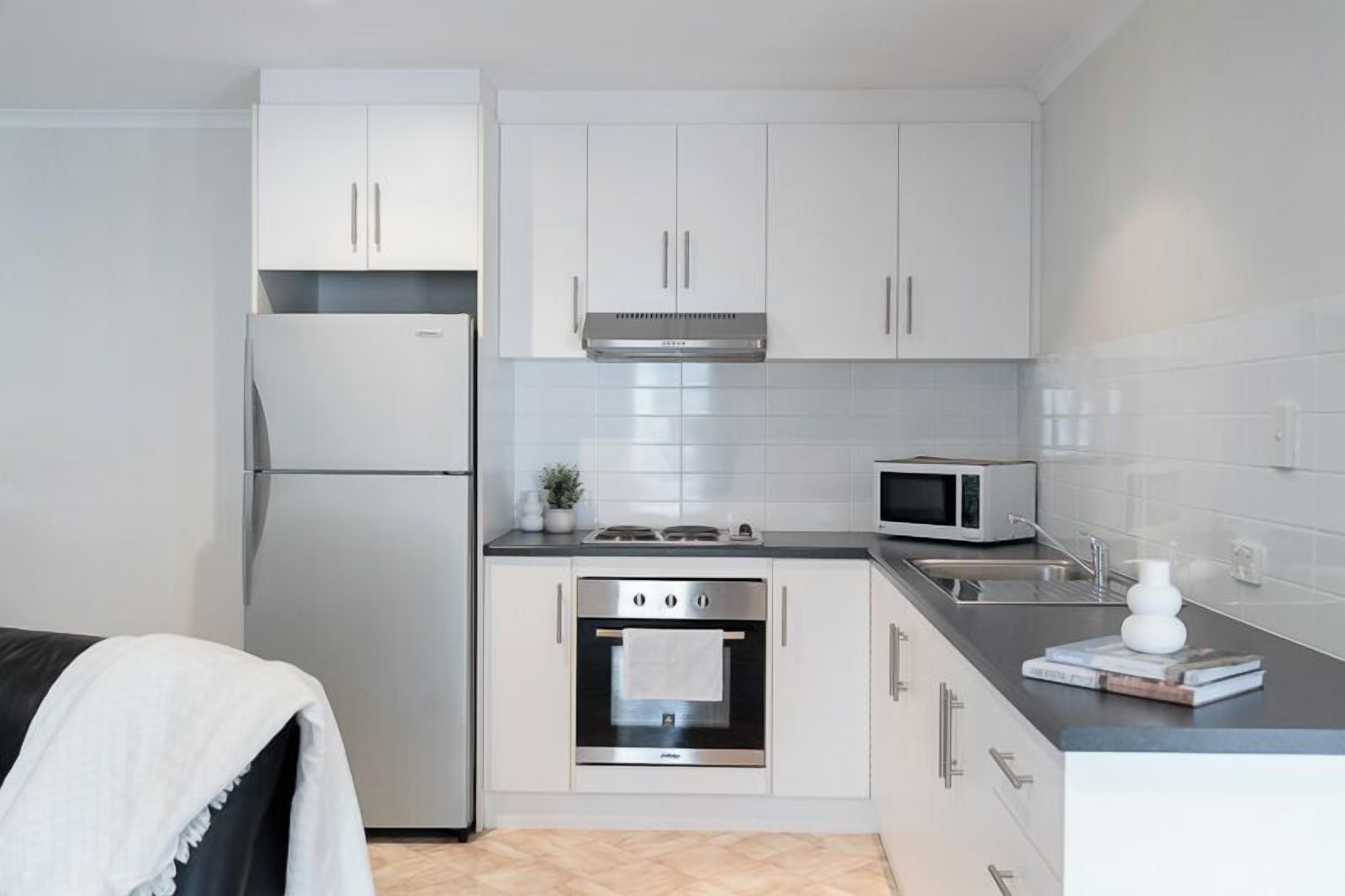 A modern kitchen with white cabinets, stainless steel appliances, and a black countertop.