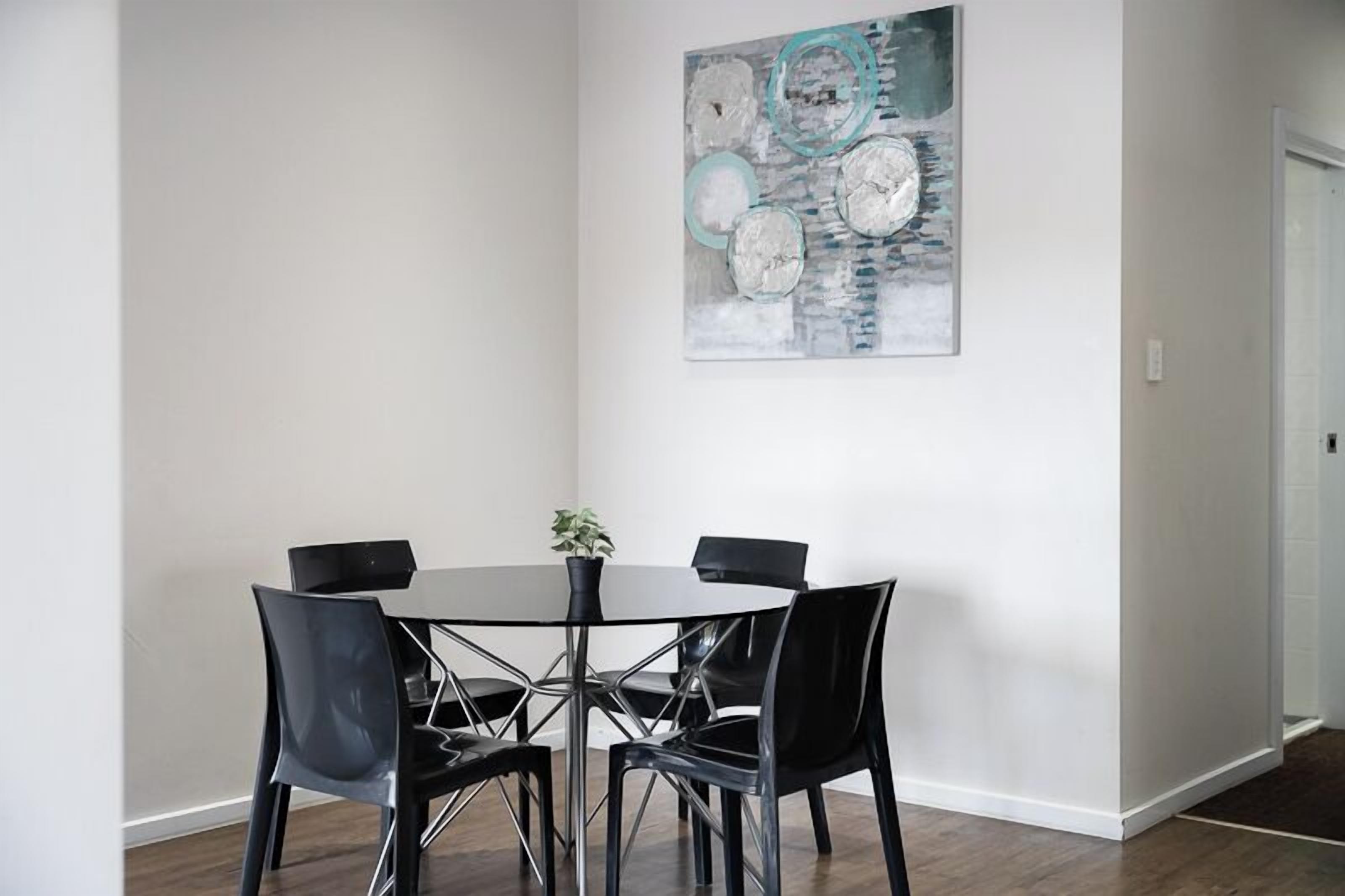 A dining area with a round table, black chairs, and a painting on the wall.