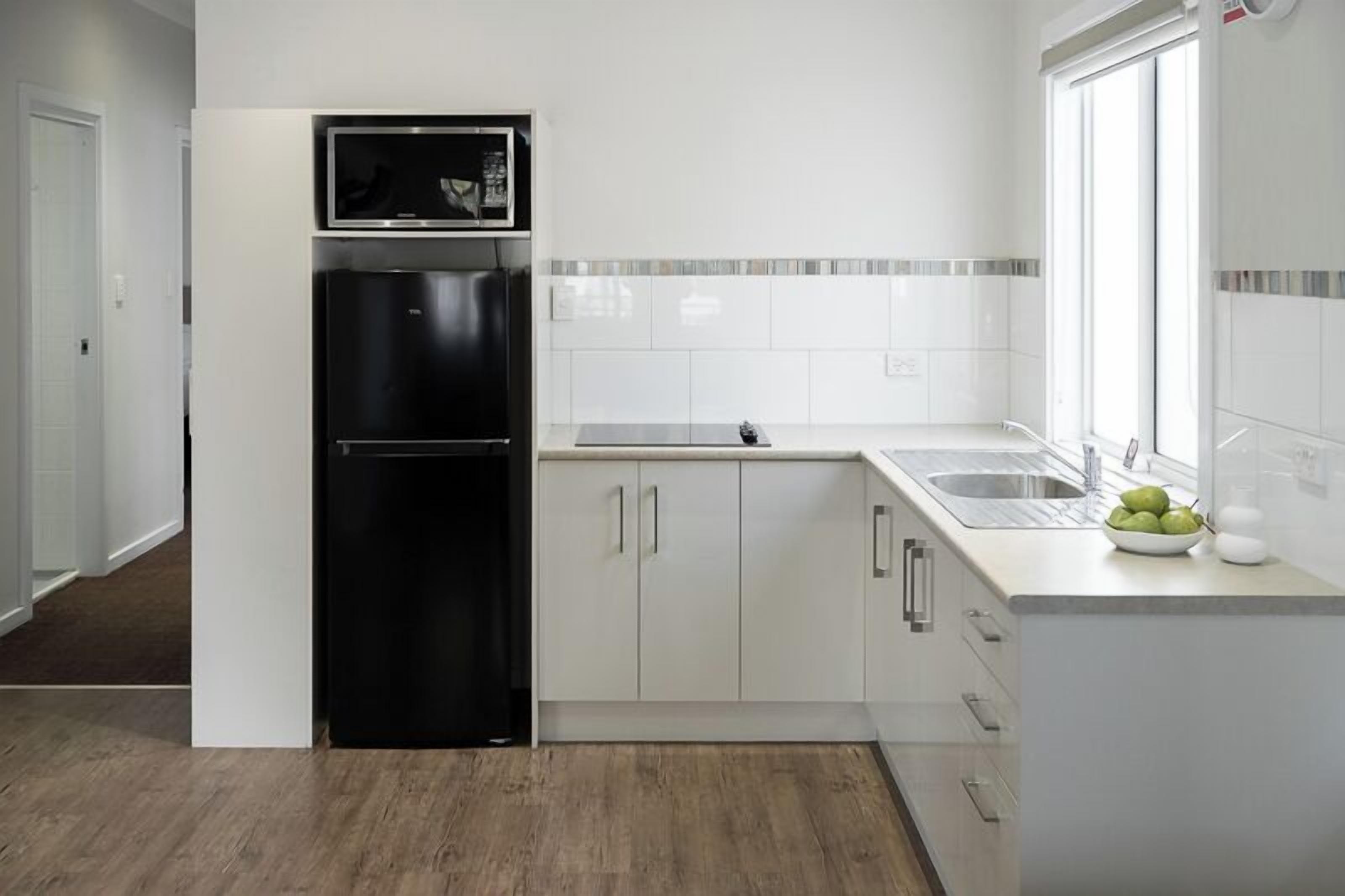 Une cuisine moderne avec des meubles blancs, un réfrigérateur noir et une fenêtre qui laisse entrer la lumière naturelle.
