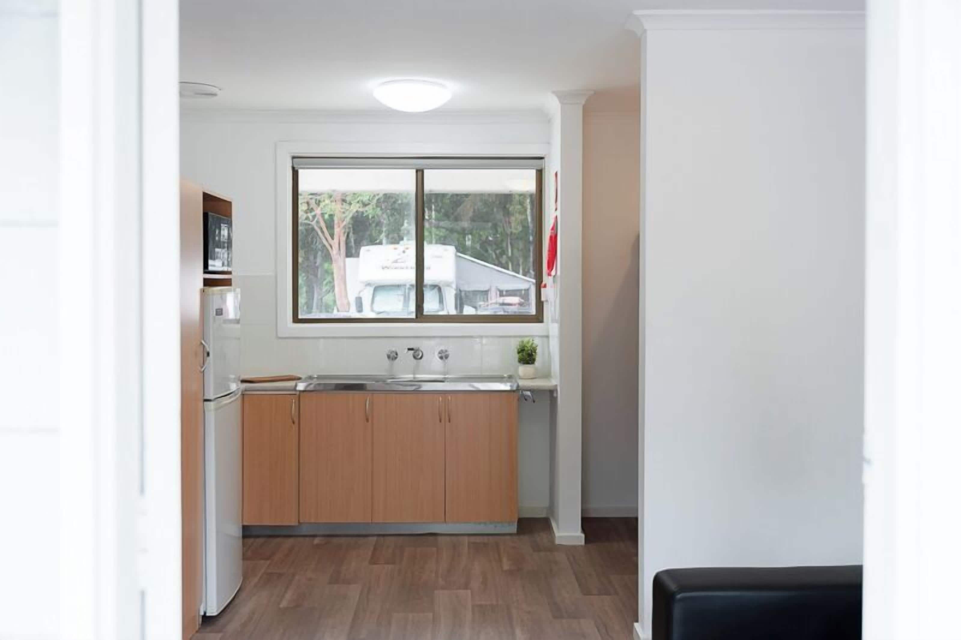 A compact kitchen with wooden cabinets, a white countertop, and a window with a view of the outside.