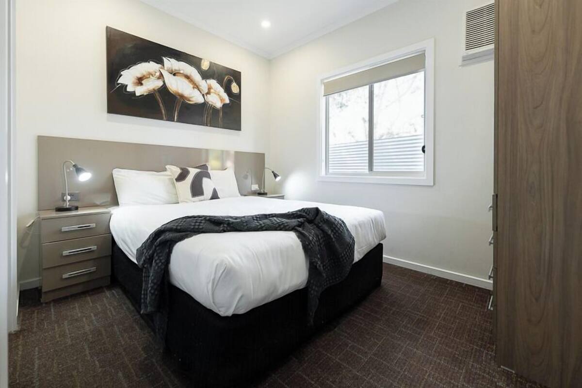 A bedroom with a bed, bedside tables, a nightstand, a window, and a painting on the wall.