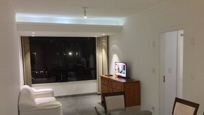 Ein modernes Hotelzimmer mit einem Glastisch, einem weißen Sofa und einem Fernseher auf einer Holzkommode.