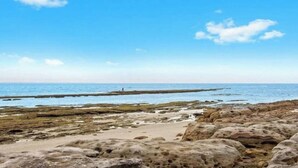 A rocky shoreline with a clear view of the sea and a distant person. - Ocean Blue Apartment Three (Currarong)
