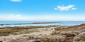 Eine felsige Küstenlinie mit freiem Blick auf das Meer und einer entfernten Person.