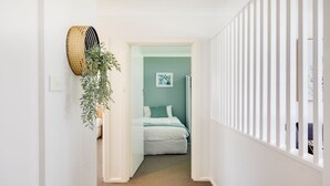 A hallway leading to a bedroom with a bed, a wall-mounted basket, and a plant. - Ocean Blue Apartment Three (Currarong)
