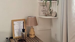 Un coin de pièce avec une petite table d’appoint en bois, une lampe, un menu encadré et des étagères ornées d’objets décoratifs et de plantes.