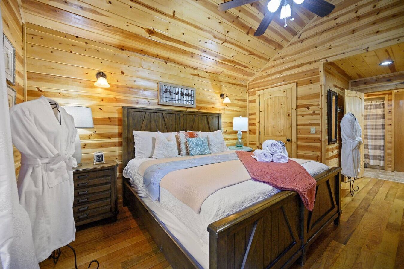 Un dormitorio tipo cabaña de madera con una cama, mesitas de noche y una bata colgada.