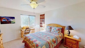 A bedroom with a bed, a desk, a chair, a nightstand, a lamp, a ceiling fan, and a window. - Adobe Dreams - 3292, Private hot tub (Moab)