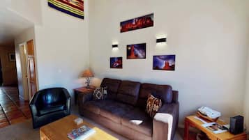 A living room with a sofa, a coffee table, a lamp, and wall-mounted artwork.